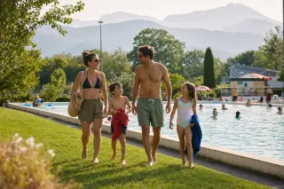Family with children enjoying the grassy area next to a public outdoor pool in Épagny Metz-Tessy, with gentle sunlight and mountain backdrop.