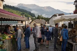 Animated village market with locals shopping and chatting among produce stalls, misty hills and forest in the background, early morning light.