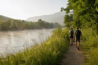 Riverside walking path near Seyssel with hikers, misty morning light over lush green vegetation and gentle Rhône river