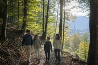 Family walking on a sun-dappled forest path in early autumn in the wooded area near Épagny Metz-Tessy, Haute-Savoie, with soft natural light filtering through beech trees.