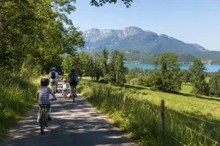 Family cycling on a scenic bike path near Épagny Metz-Tessy with Lake Annecy and wooded hills in the background under gentle summer sunlight