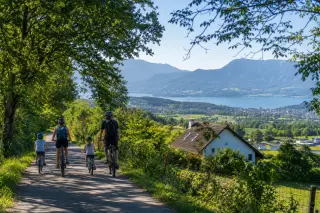 Family cycling on a shaded path in Épagny Metz-Tessy with hills and Lake Annecy in the background, under gentle morning light