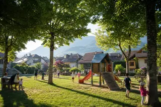 Children playing in a leafy communal park, soft morning light, parents nearby, tiled village roofs and tree-covered hills in the background, casual and authentic alpine atmosphere.
